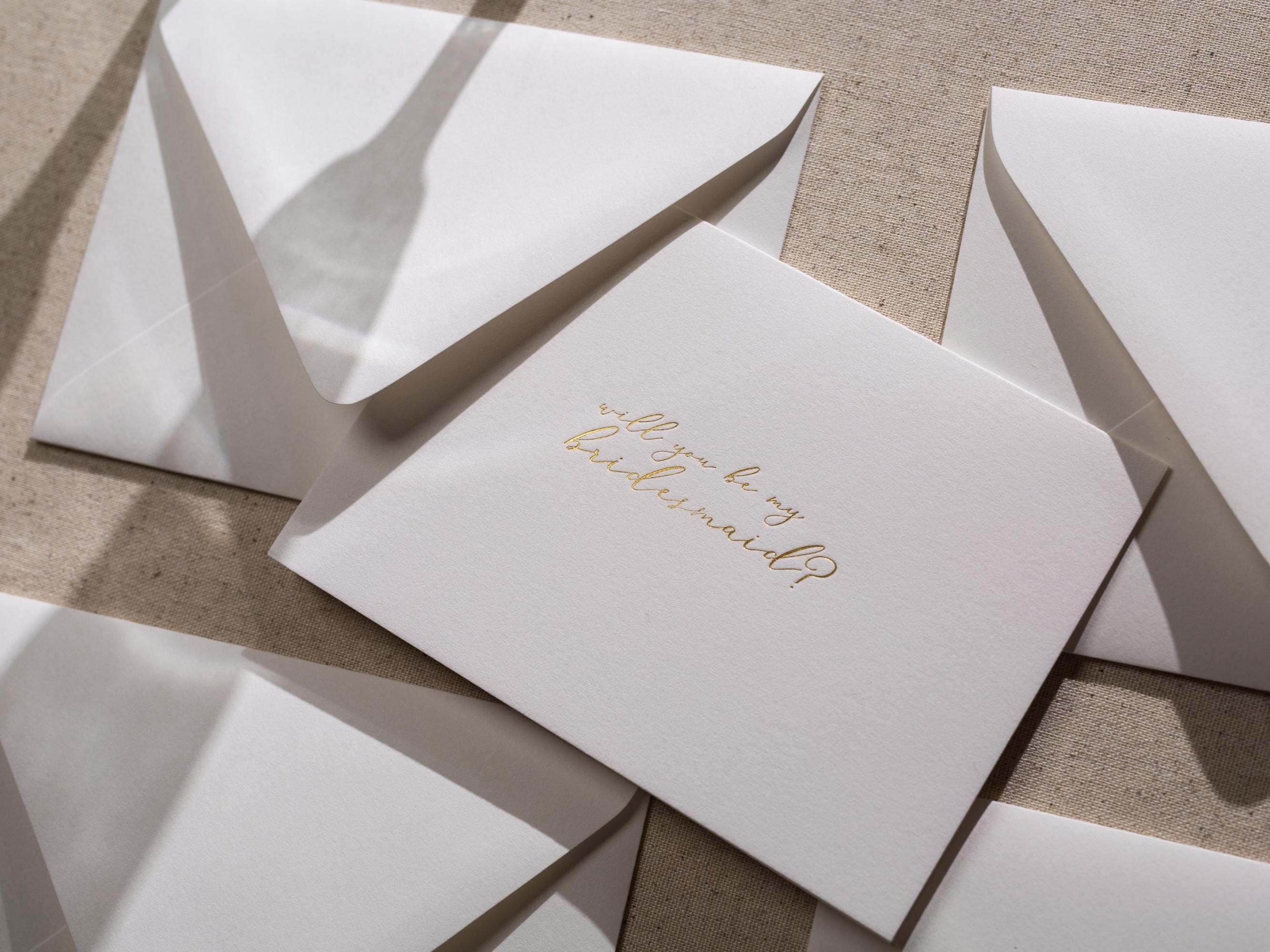 May include: A white card with gold foil lettering that says &#39;Will you be my bridesmaid?&#39;