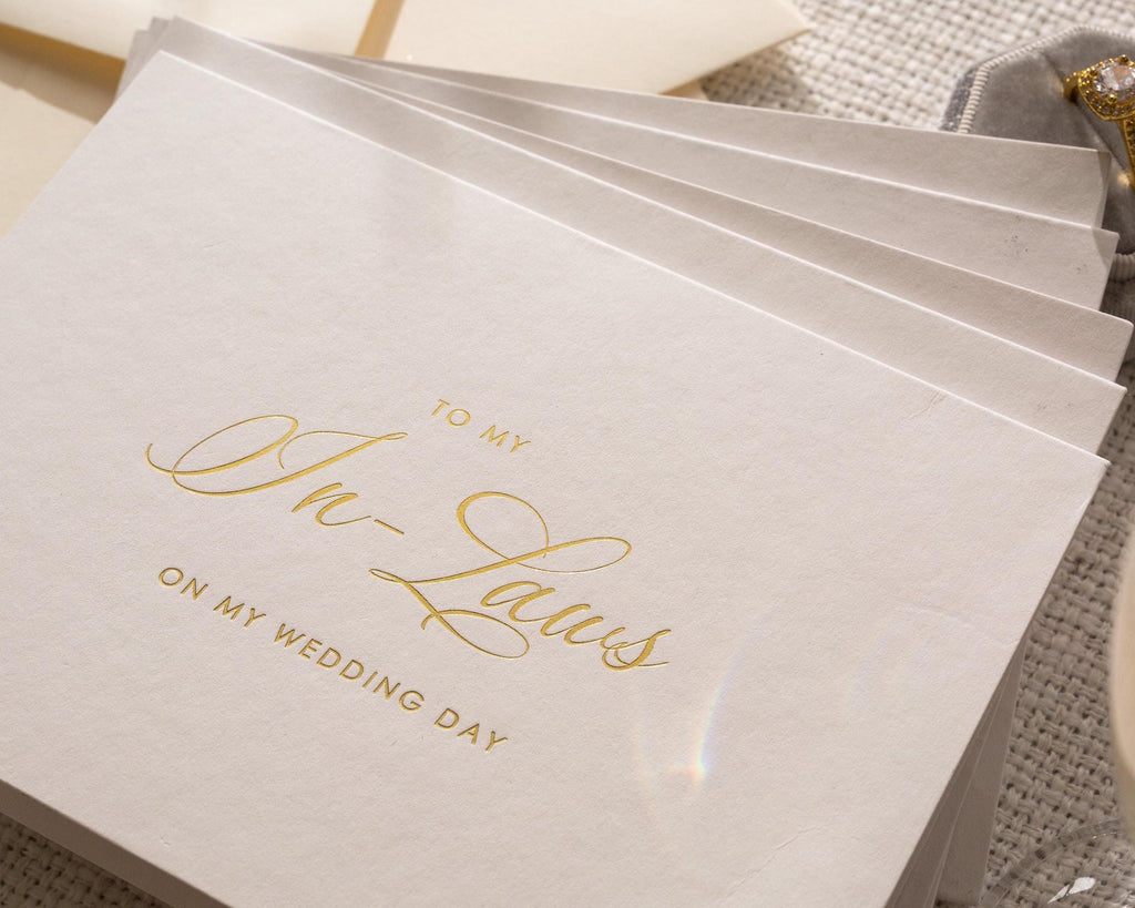 May include: A stack of ivory-colored cards with gold script. The text reads "TO MY In-Laws ON MY WEDDING DAY". The cards are arranged in a fan shape, suggesting a stationery set for a wedding.