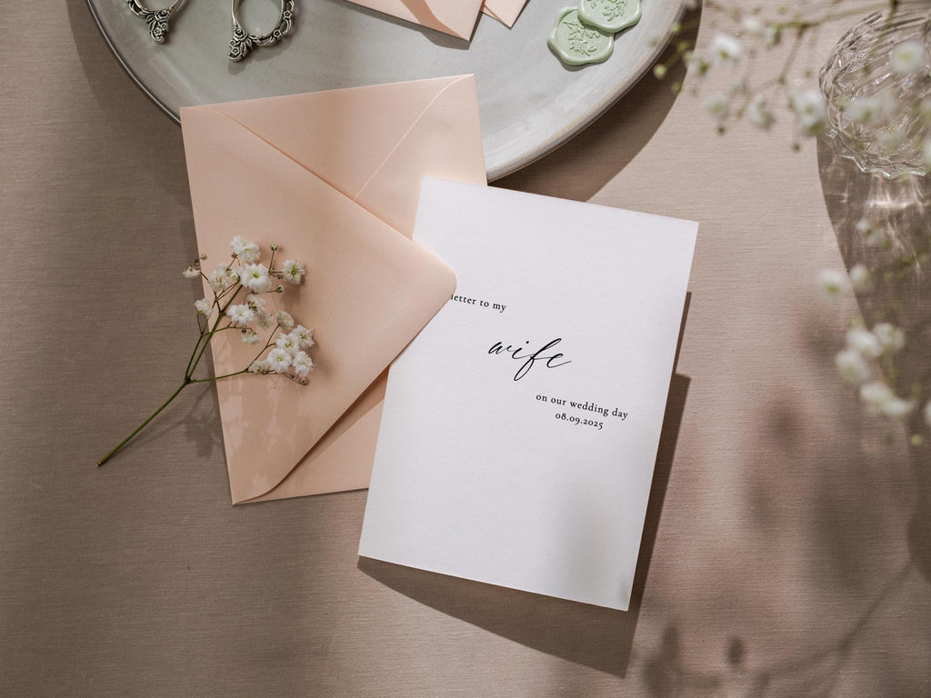 May include: A white card with black calligraphy that reads "Letter to my wife on our wedding day 08.09.2023". The card is on a light pink envelope and a light brown surface.