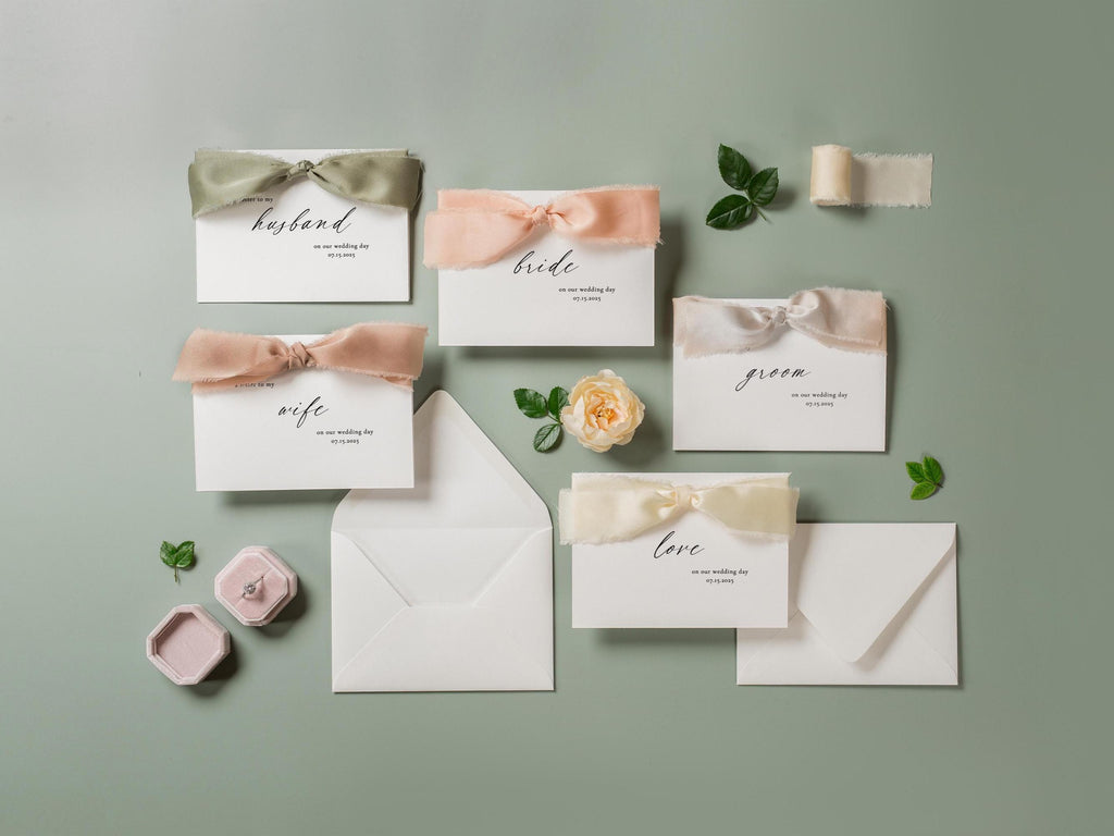 May include: A set of six wedding cards with different titles, including "husband", "wife", "bride", "groom", "love", and a blank card. Each card is decorated with a satin ribbon bow in a different color, including green, pink, and beige. The cards are arranged on a light green background.