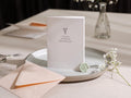 May include: A white card with a floral design and the text "EVELYN, will you be my BRIDESMAID?" on it. The card is on a light gray plate with a green wax seal.