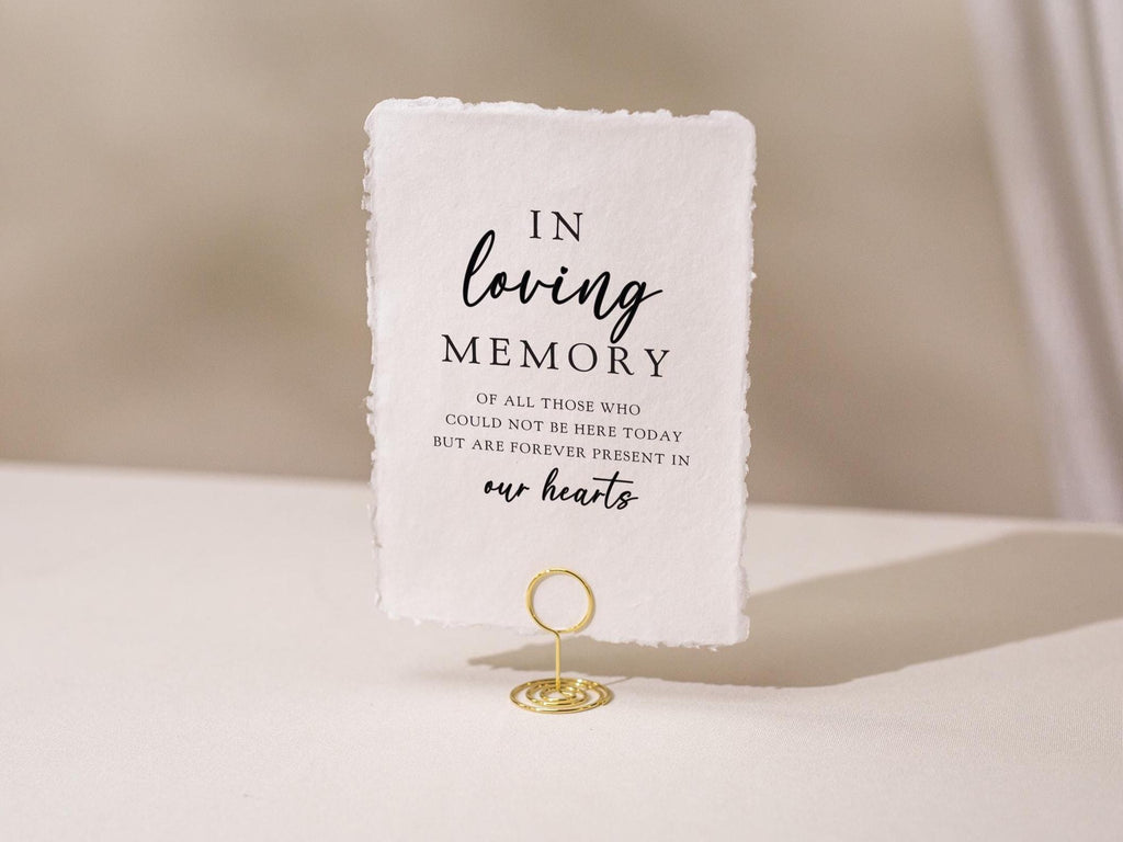 May include: A white rectangular sign with the text "IN loving MEMORY" in black script. The sign is held by a gold wire holder. The text continues with "OF ALL THOSE WHO COULD NOT BE HERE TODAY BUT ARE FOREVER PRESENT IN our hearts."