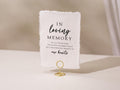 May include: A white rectangular sign with the text "IN loving MEMORY" in black script. The sign is held by a gold wire holder. The text continues with "OF ALL THOSE WHO COULD NOT BE HERE TODAY BUT ARE FOREVER PRESENT IN our hearts."