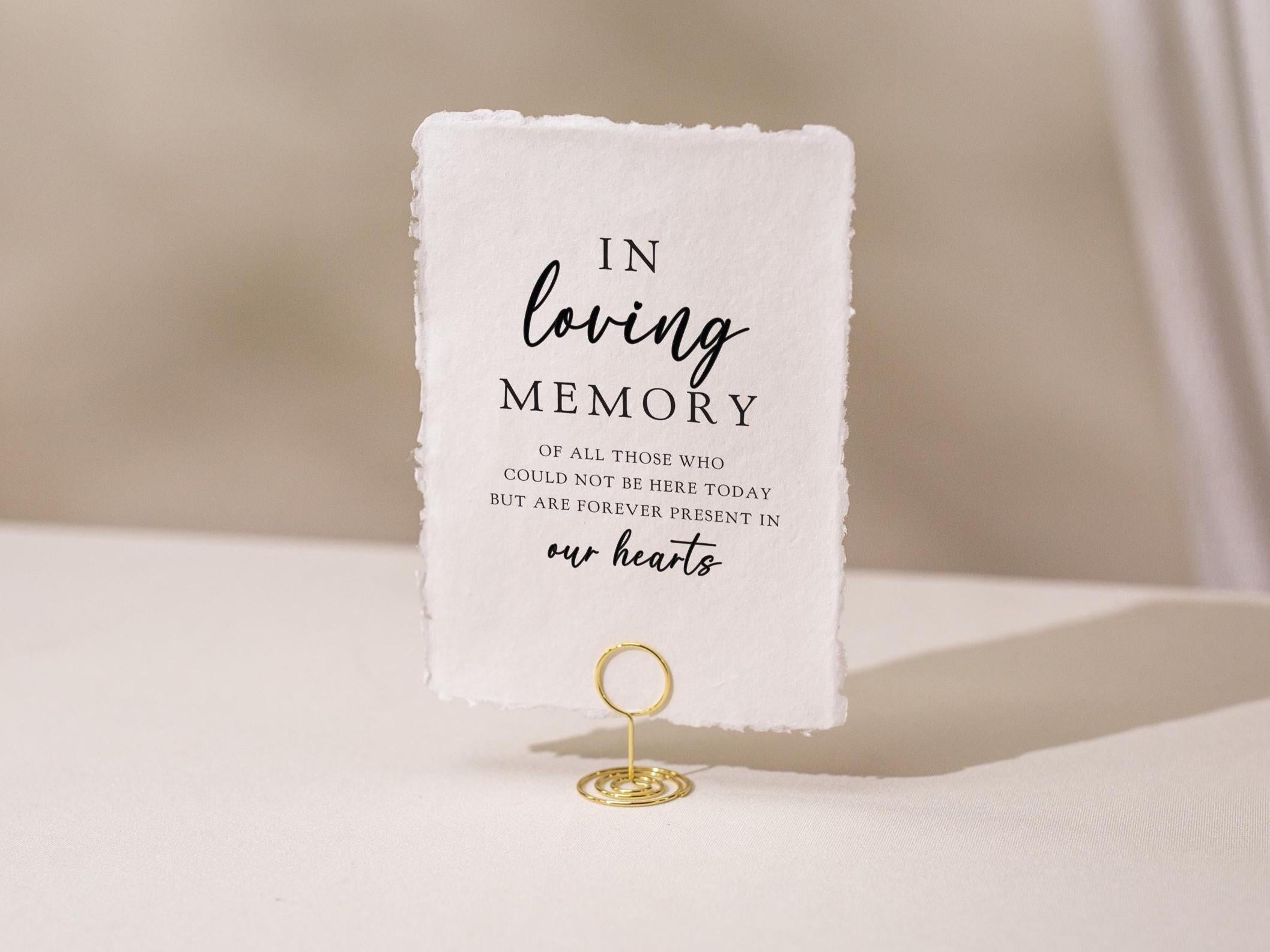 May include: A white rectangular sign with the text "IN loving MEMORY" in black script. The sign is held by a gold wire holder. The text continues with "OF ALL THOSE WHO COULD NOT BE HERE TODAY BUT ARE FOREVER PRESENT IN our hearts."