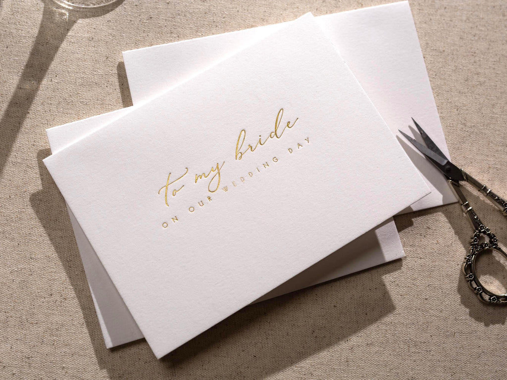 May include: A white card with gold foil lettering that reads "to my bride on our wedding day".