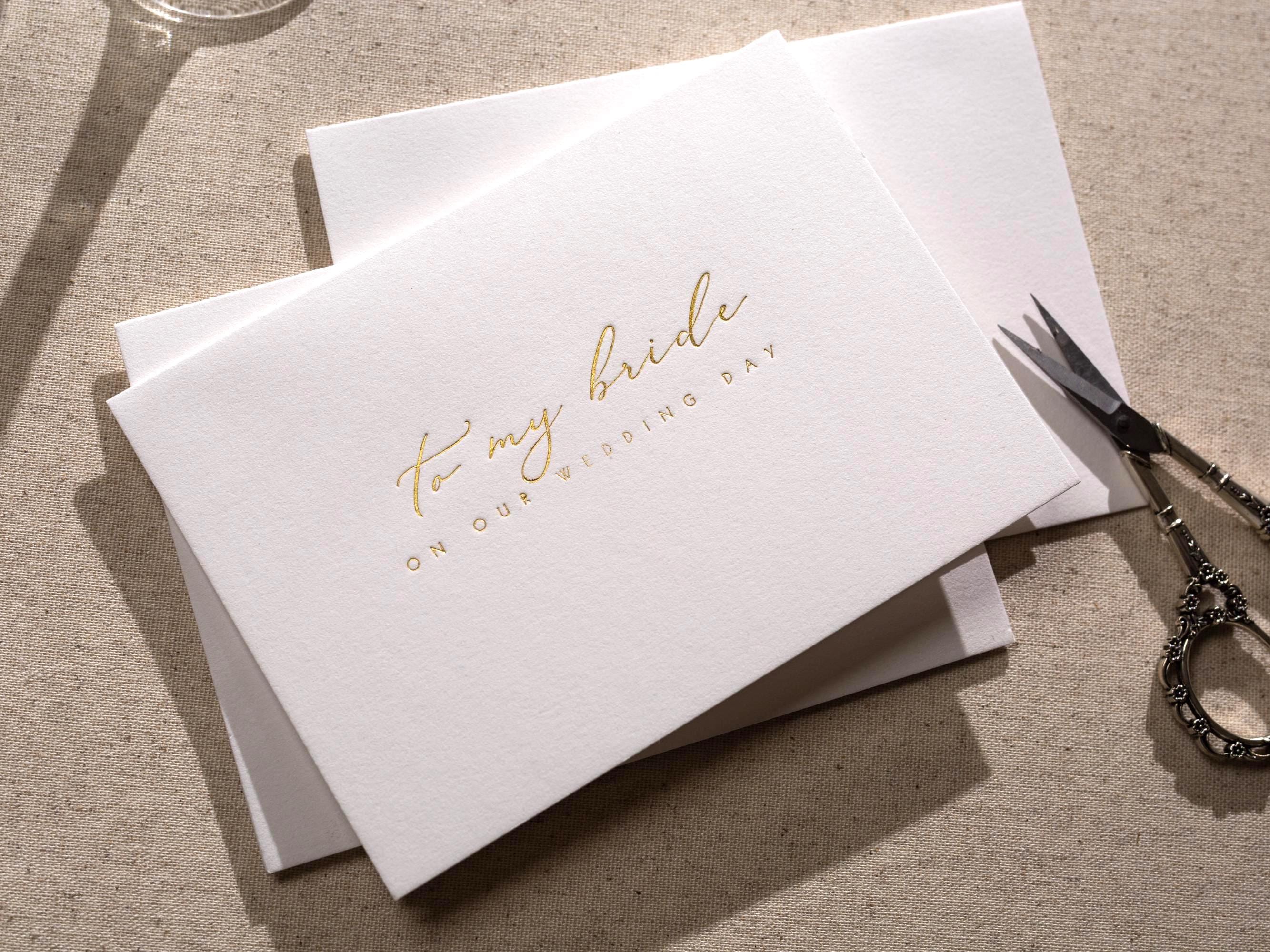 May include: A white card with gold foil lettering that reads "to my bride on our wedding day".