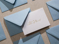 May include: A white card with gold lettering that says "Will you be my matron of honor?" The card is surrounded by light blue envelopes.