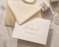 May include: A cream-colored wedding card and envelope with gold script that reads "To My Bridesmaid On My Wedding Day." A ring box and pearl necklace are also visible.