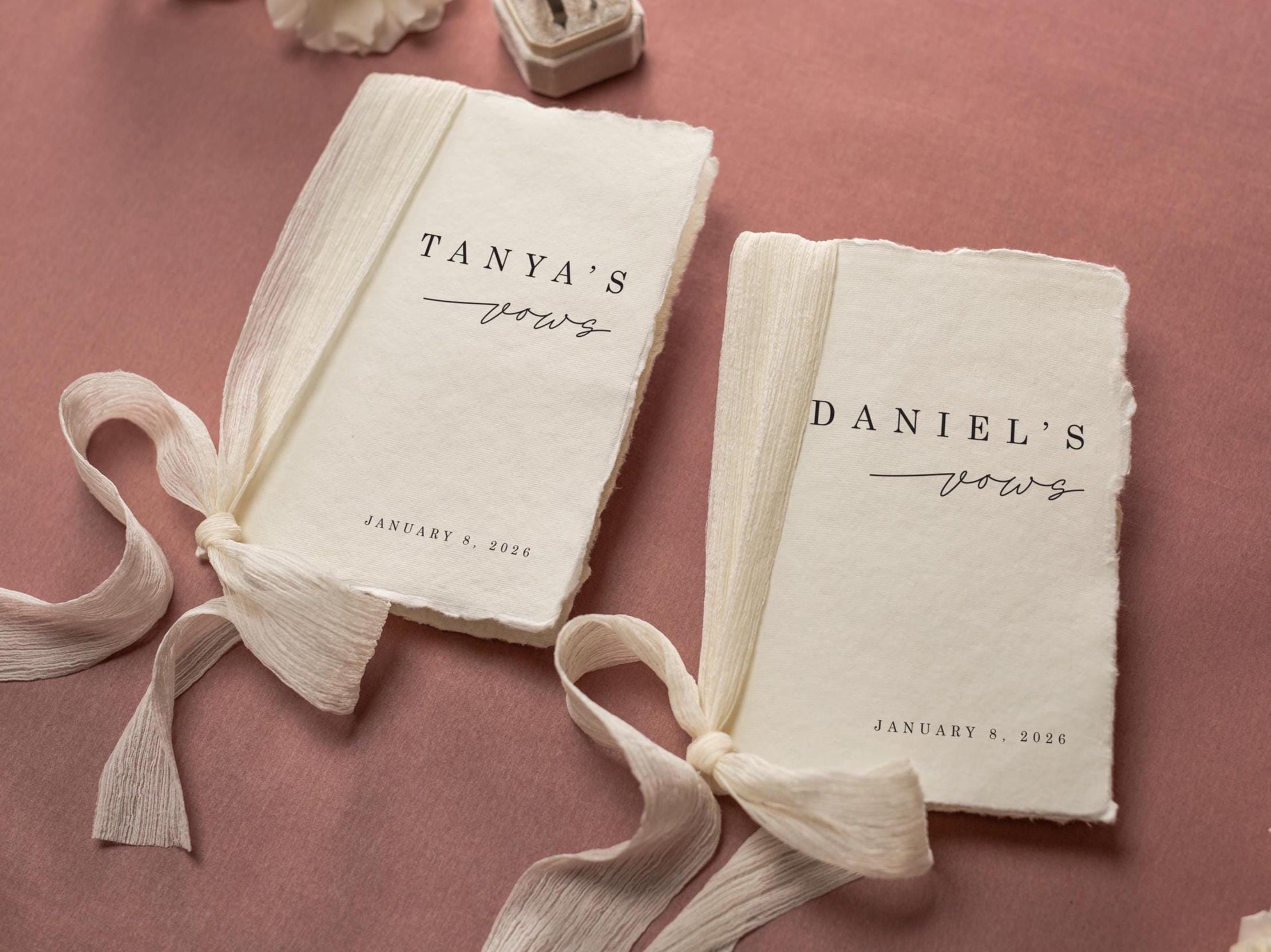 May include: Two vow books with deckled edges, tied with cream-colored ribbons. The text "Tanya's vows" and "Daniel's vows" are printed in black script, along with the date January 8, 2026. The background is a muted rose color.