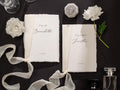 May include: Two white paper vow books with a white ribbon tied around them. The books have the text "to my wife Bernadette" and "to my husband Jonathan" written on them. The date "11.12.2023" is written on both books.